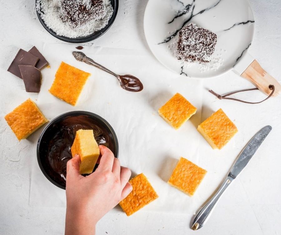 Lamington sẽ được nhúng vào hỗn hợp Chocolate frosting và phủ thêm lớp cơm dừa sấy khô bên ngoài  